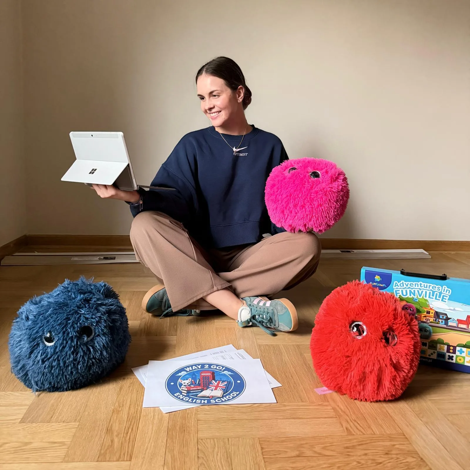 Kasia, lektorka Way2Go, siedzi na podłodze z tabletem, maskotkami Fuzzy Friends i materiałami szkolnymi
